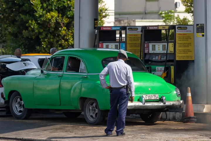 Un policía (de espaldas) observa a un coche antiguo en una gasolinera, hoy en La Habana (Cuba). EFE/Yander Zamora