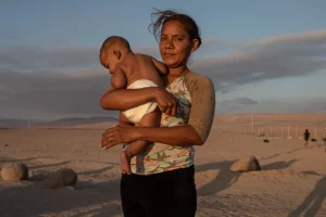 Jimir Coromoto sostiene a su hijo mientras esperan soluciones a su situación migratoria, en el paso fronterizo Chacalluta, en Arica (Chile). EFE/Lucas Aguayo Araos