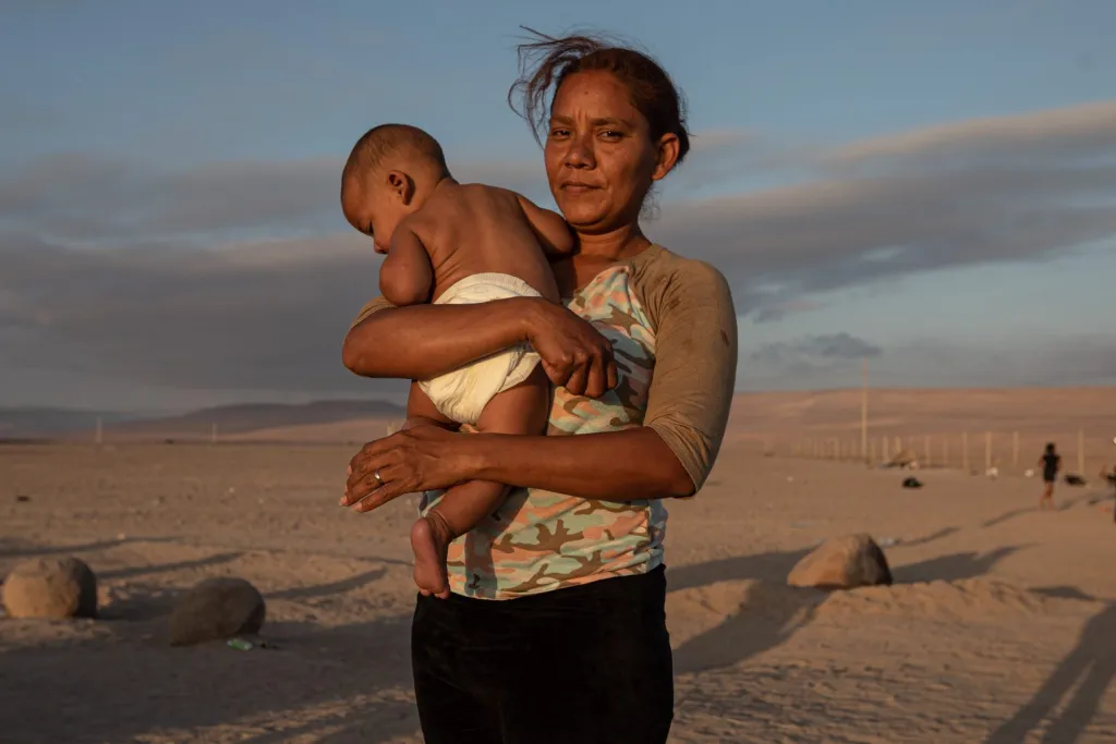 Jimir Coromoto sostiene a su hijo mientras esperan soluciones a su situación migratoria, en el paso fronterizo Chacalluta, en Arica (Chile). EFE/Lucas Aguayo Araos