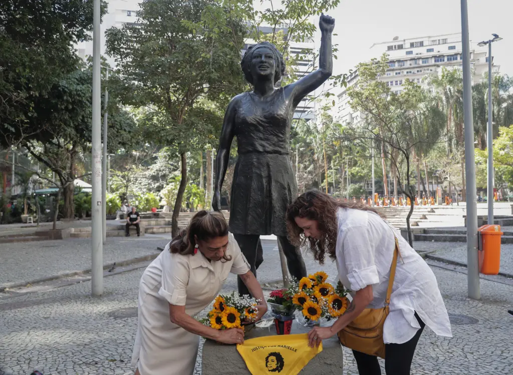 Mônica Benício (d) y Marinete da Silva (i), viuda y madre, respectivamente, de la concejala asesinada Marielle Franco, colocan flores y un pañuelo en su estatua durante un homenaje por el día de su cumpleaños, en Río de Janeiro (Brasil). EFE/André Coelho