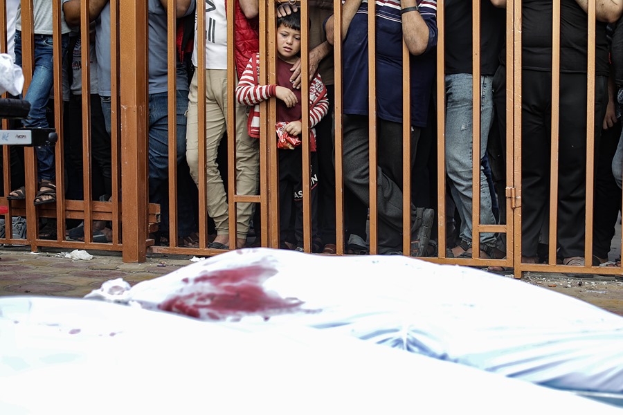 Un niño palestino observa tras unos barrotes los cadáveres de las víctimas cubiertos con sábanas en el hospital Nasser en Jan Yunis, al sur de la Franja de Gaza. EFE/ Haitham Imad