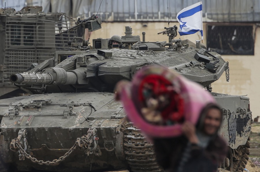 Palestinos desplazados internamente pasan junto a los tanques israelíes en el campamento de Juan Yunis. EFE/EPA/Mohammed Saber