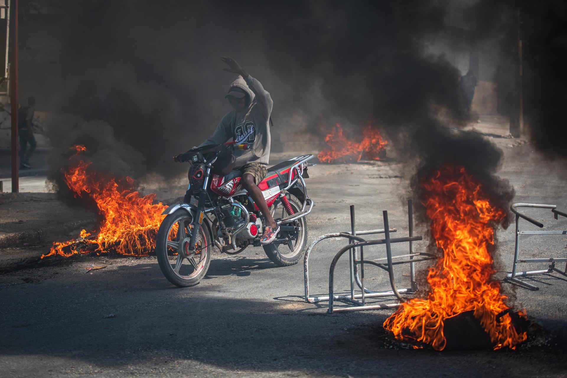 Una persona se transporta en motocicleta con incendios alrededor, en Puerto Príncipe (Haití). EFE/Johnson Sabin