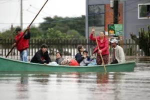 Varias personas esperan junto a unos vehículos atrapados en una zona inundada por las lluvias este viernes, en Porto Alegre (Brasil). EFE/ Renan Mattos