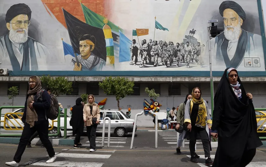 Ciudadanos iraníes en una calle de Teherán sobre la que se alza un mural con la imagen del líder supremo iraní, el ayatollah Ali Jamenei i) y el difunto líder supremo, el ayatollah Jomeini (d). EFE/EPA/Abedin Taherkenareh